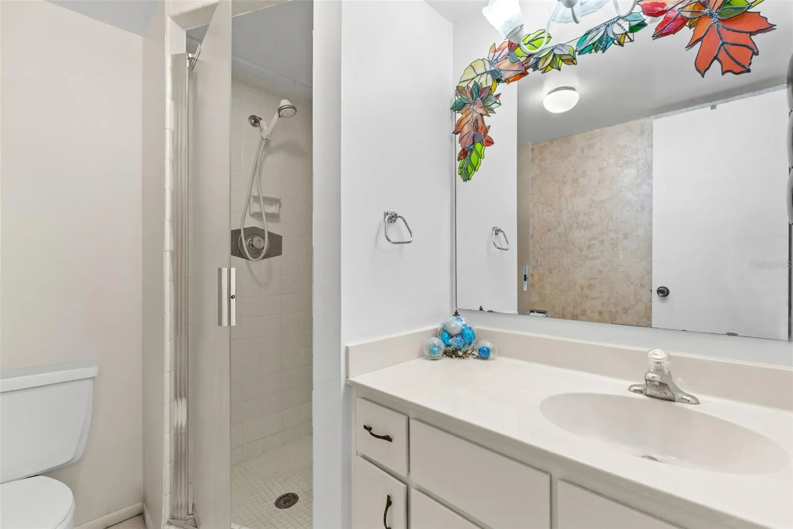 Bedroom 2 has its own ensuite bath with a single-sink vanity, generous counter space and a large wall mirror. The walk-in shower includes a glass door, tiled surround and handheld showerhead.