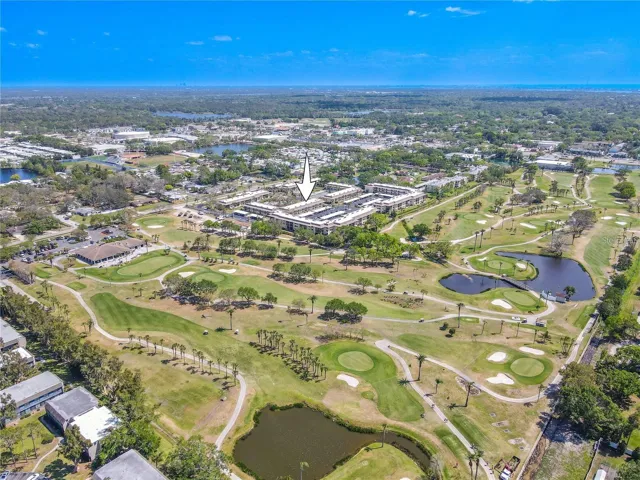 Villas de Golf is arranged around landscaped grounds with the community pool and tennis courts near the center, while the neighboring golf course stretches along the east side of the property and the Gulf sits in the distance.