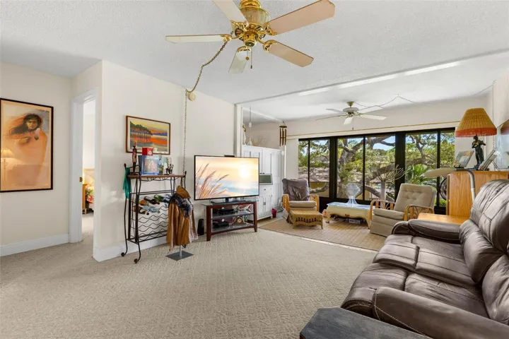 The living room opens directly into the enclosed Florida room, creating a second sitting area framed by a broad wall of windows. Neutral carpeting continues through both spaces, while ceiling fans add comfort overhead.