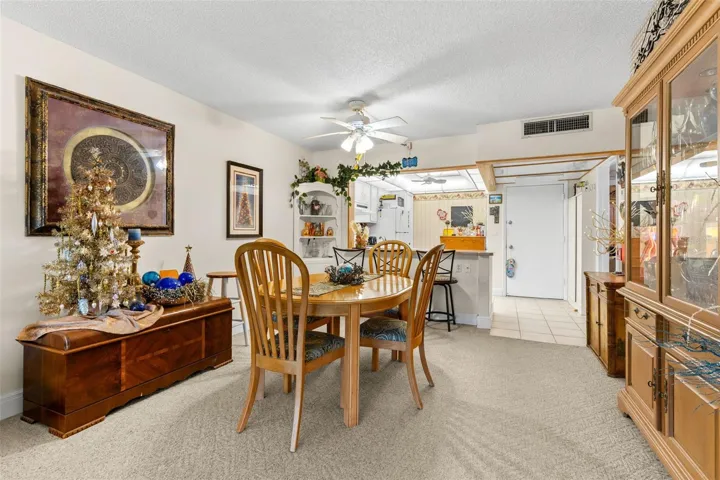 Neutral carpeting and soft wall tones keep the dining area understated, while a ceiling fan adds practical comfort. The open connection to the kitchen keeps the space visually linked without losing its own defined footprint.