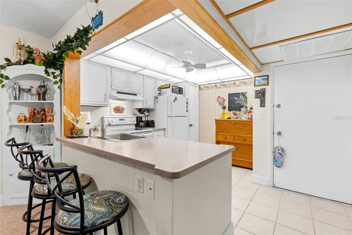 Just inside the entry, the kitchen wraps around a wide peninsula with bar seating, generous counter space and open shelving nearby. The raised ceiling detail continues overhead, while the open layout keeps the kitchen connected to the dining and living areas beyond.