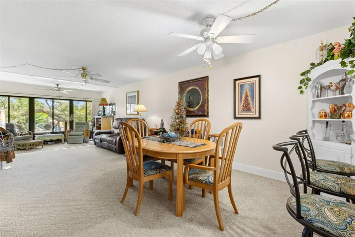 The dining area sits between the kitchen and living room, creating a long, open main living space with plenty of room to define each area. A wall of windows at the far end brings in natural light and looks out toward the trees and landscaped grounds.