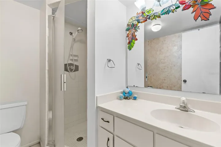 Bedroom 2 has its own ensuite bath with a single-sink vanity, generous counter space and a large wall mirror. The walk-in shower includes a glass door, tiled surround and handheld showerhead.