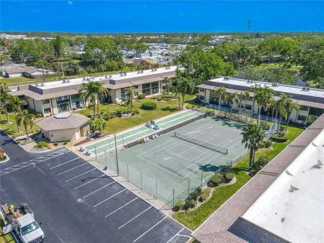 The recreation area includes a full tennis court with adjacent shuffleboard courts, set among palms and landscaped grounds near the center of the community.