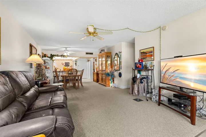 The main living area runs in one continuous line from the living room through the dining space to the kitchen, giving each area its own place without closing them off from one another. Neutral carpeting and ceiling fans continue throughout the shared living space.