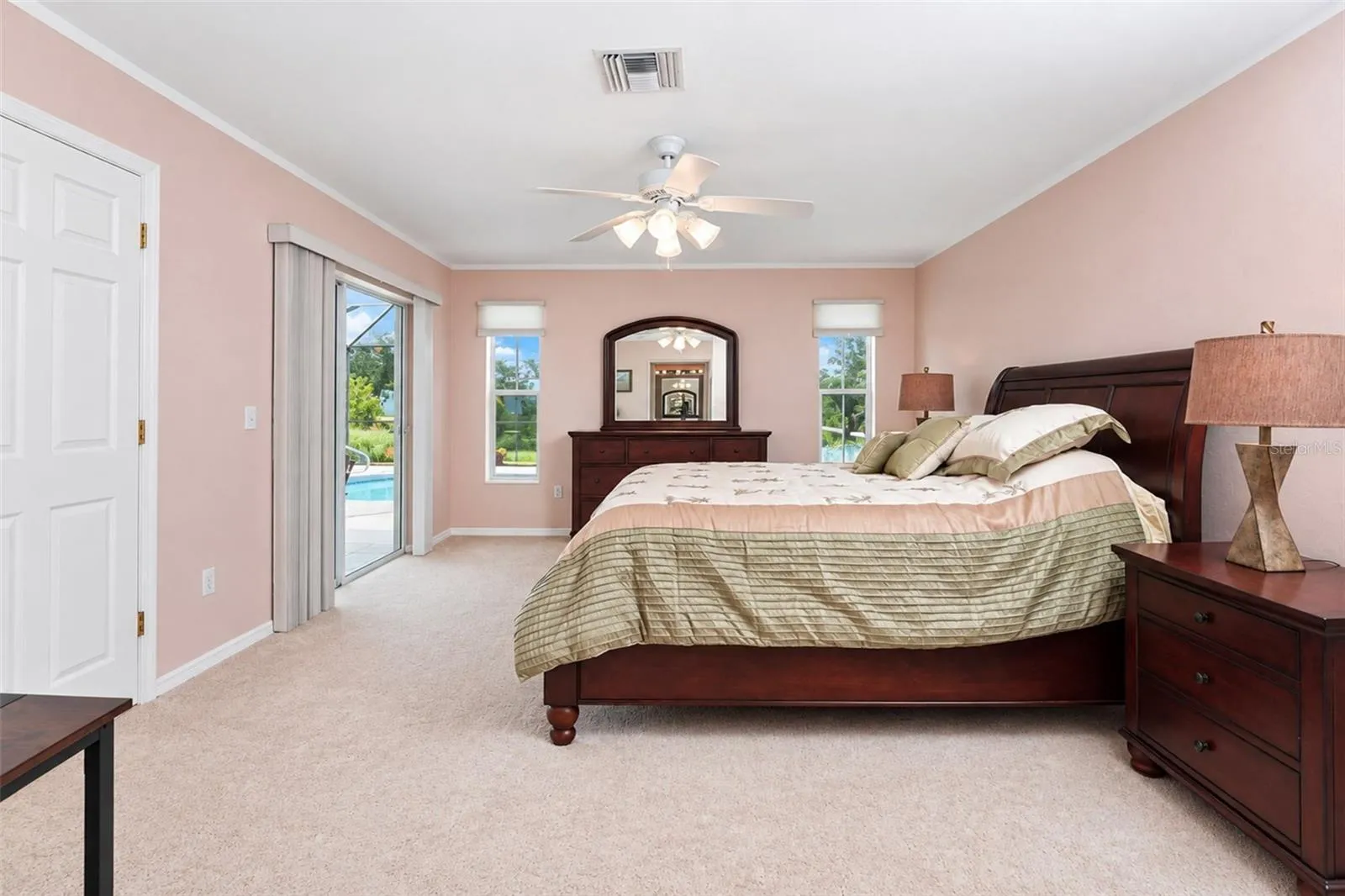 The primary bedroom has carpeted flooring, a ceiling fan and sliding glass doors to the lanai & pool.