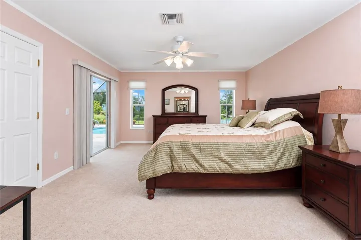 The primary bedroom has carpeted flooring, a ceiling fan and sliding glass doors to the lanai & pool.