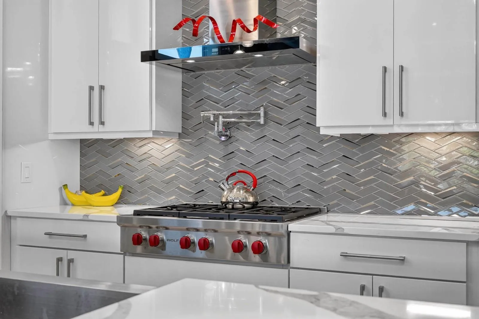 Wolf gas range, pot filler, custom cabinetry and a striking herringbone backsplash pair professional-grade function with polished design.