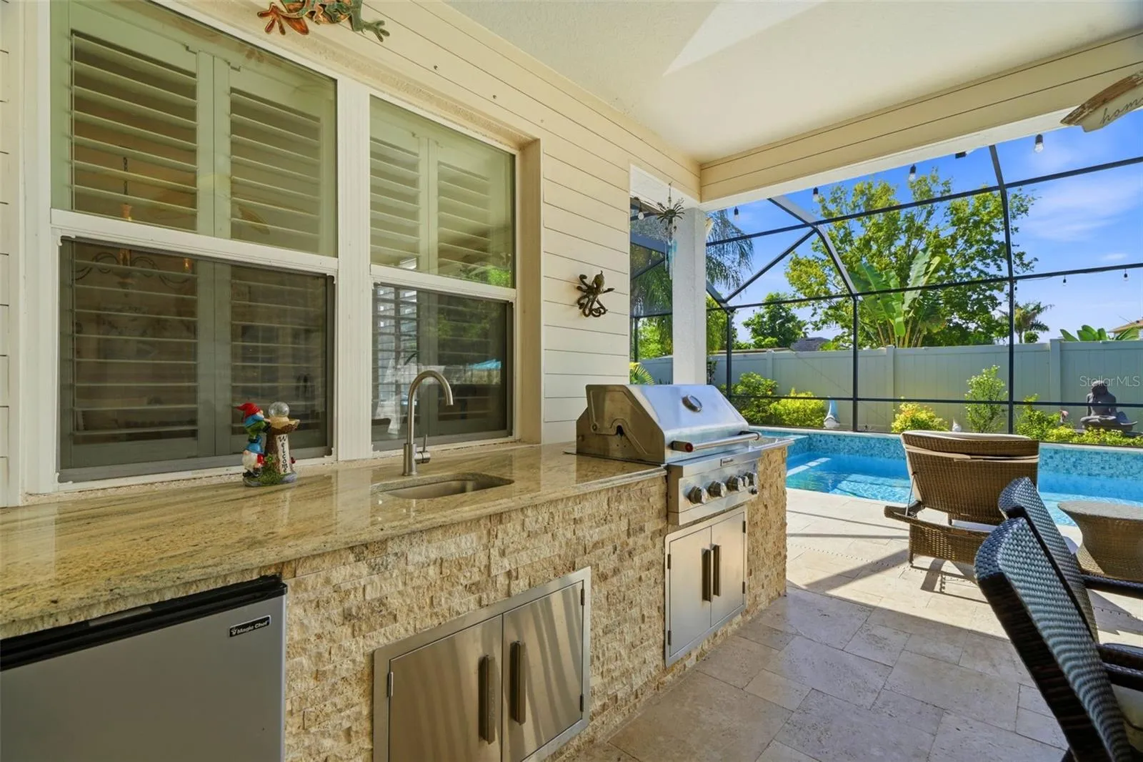 Custom outdoor kitchen with granite countertop, built-in grill, refrigerator and sink.