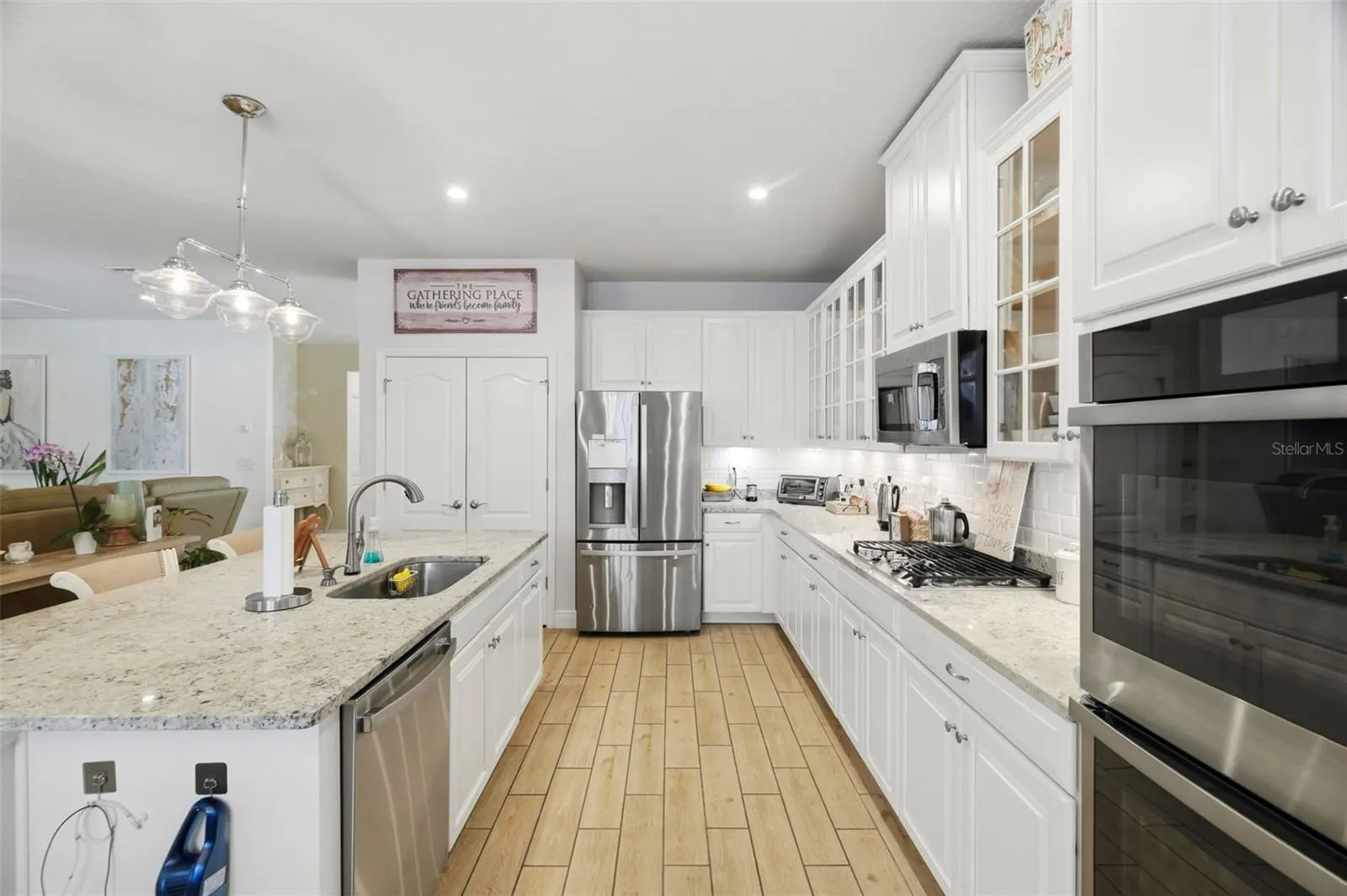 Open-concept kitchen with granite countertops, oversized island, stainless steel appliances, double wall ovens and glass-front cabinetry.