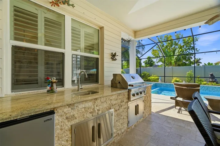 Custom outdoor kitchen with granite countertop, built-in grill, refrigerator and sink.
