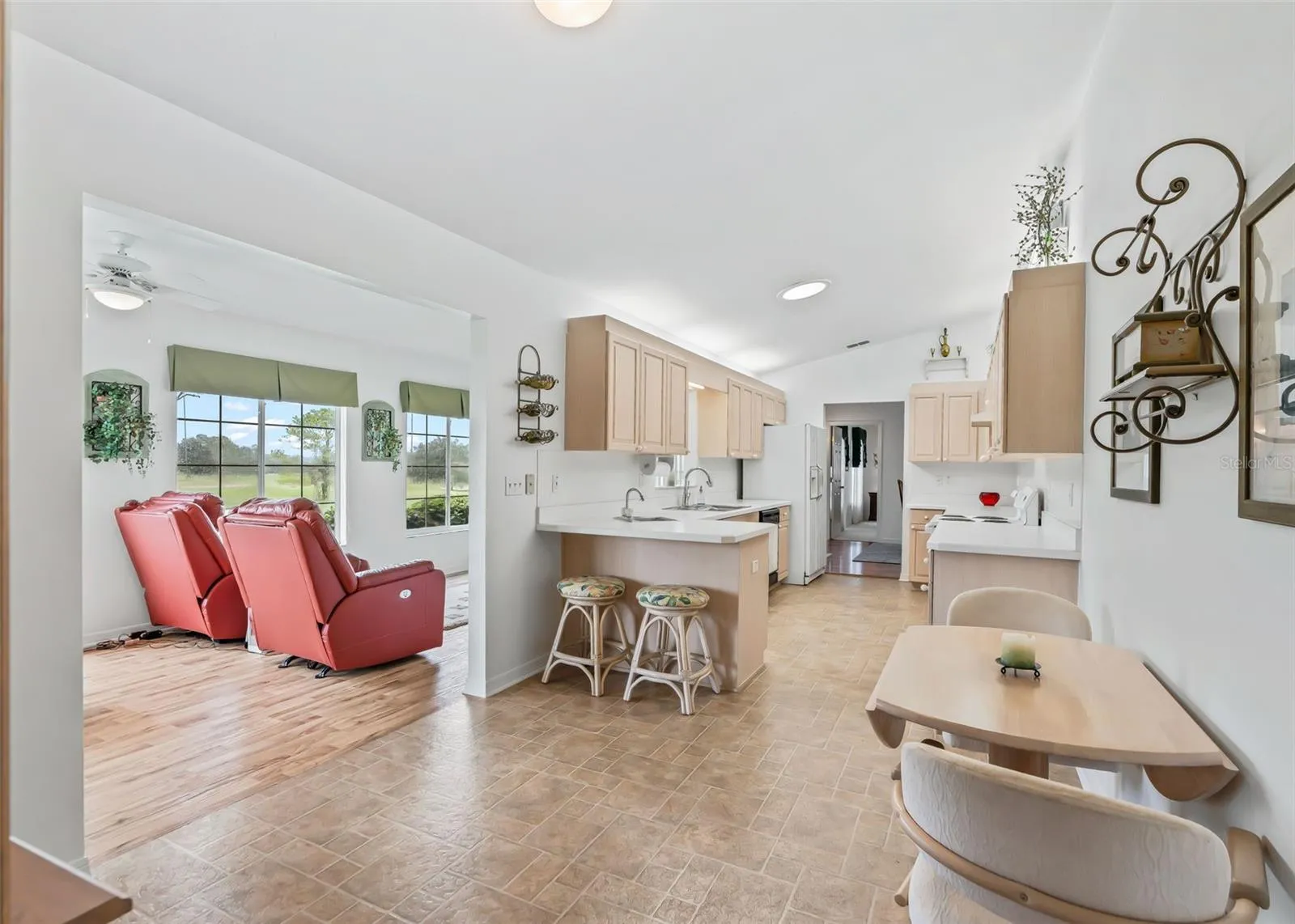 Bright, spacious kitchen featuring ample cabinetry and generous counter space, with a convenient breakfast bar for casual dining. The kitchen flows seamlessly into the adjoining living area, creating an open and inviting layout. Large windows in the living space bring in plenty of natural light and offer a beautiful view of the surrounding landscape. The adjacent dining area provides a comfortable space for everyday meals and entertaining.