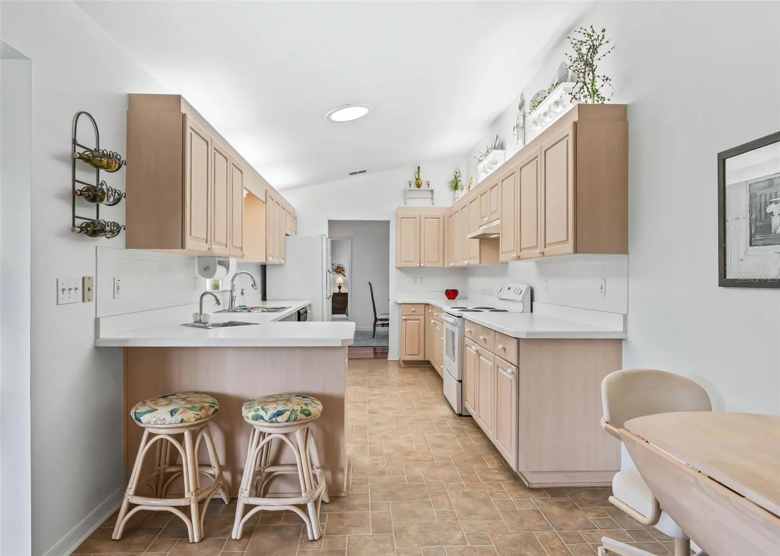 Spacious and bright kitchen featuring abundant cabinetry, generous counter space, and a convenient eat-at breakfast bar with seating. The skylight fills the kitchen with natural light, while the double sink and functional layout provide plenty of workspace for everyday cooking and entertaining