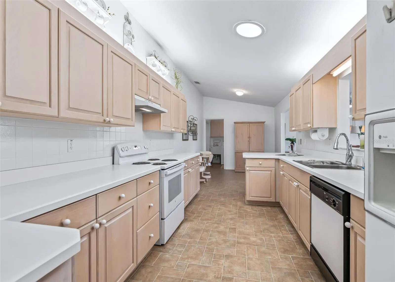 Large, bright galley-style kitchen featuring white appliances and plenty of cabinetry for ample storage. The functional layout provides a comfortable space for meal preparation, casual dining, and entertaining.