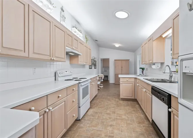 Large, bright galley-style kitchen featuring white appliances and plenty of cabinetry for ample storage. The functional layout provides a comfortable space for meal preparation, casual dining, and entertaining.