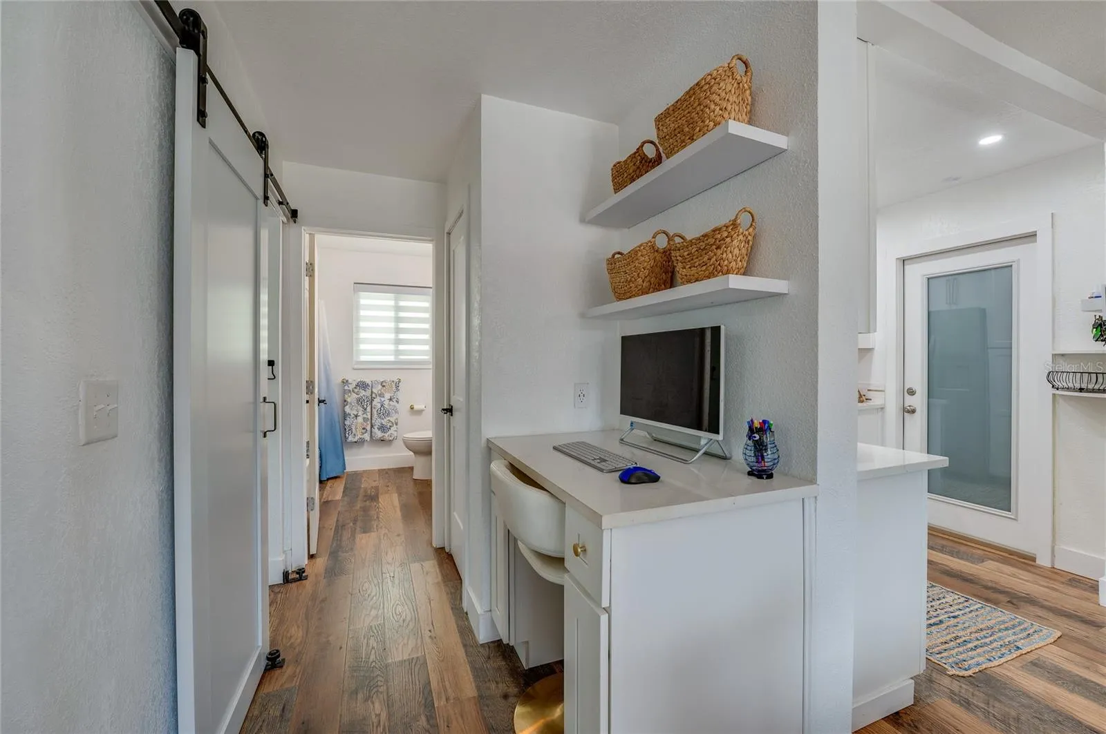 Built-in study alcove with white cabinetry, quartz counter space, and floating shelves, situated in a hallway featuring LVP floors and a sliding barn door.