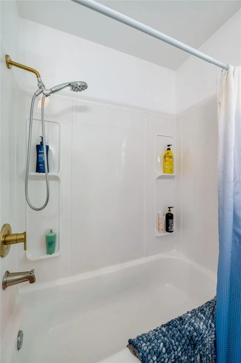 Close-up of a updated bathtub and shower combination complete with a white surround, dual wall niches for toiletries, and warm gold hardware.