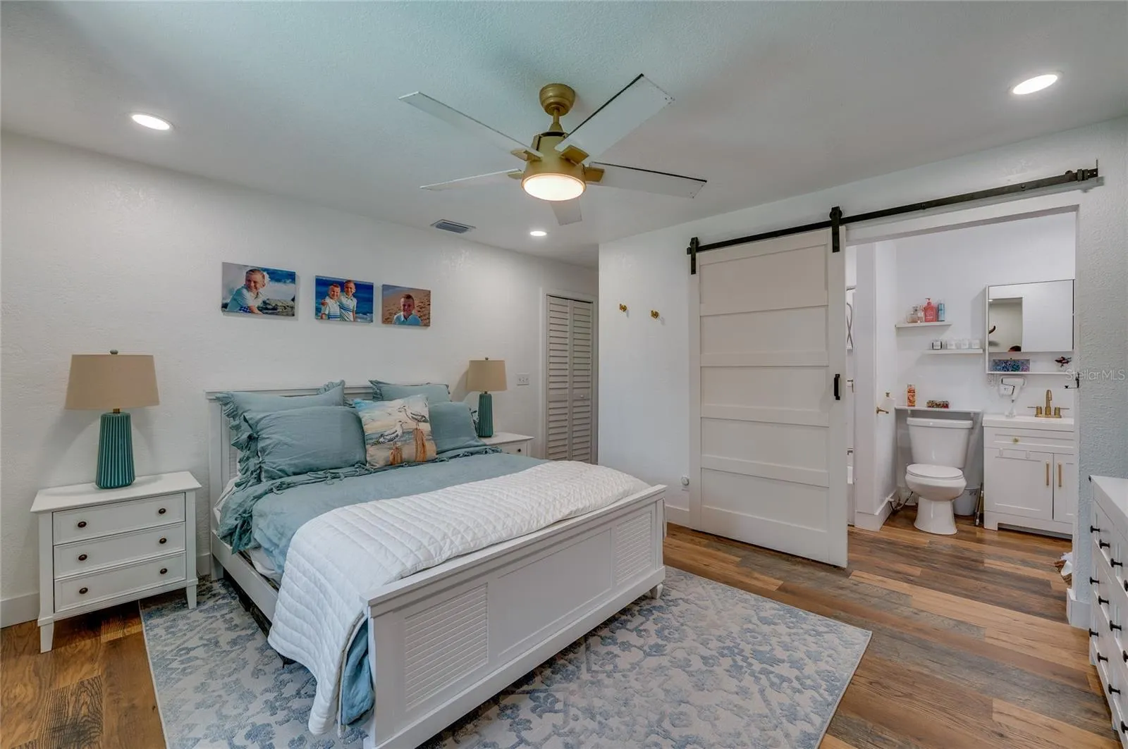 Spacious primary bedroom suite showcasing warm LVP flooring, a ceiling fan, and direct access to an ensuite bathroom through a sliding white barn door.