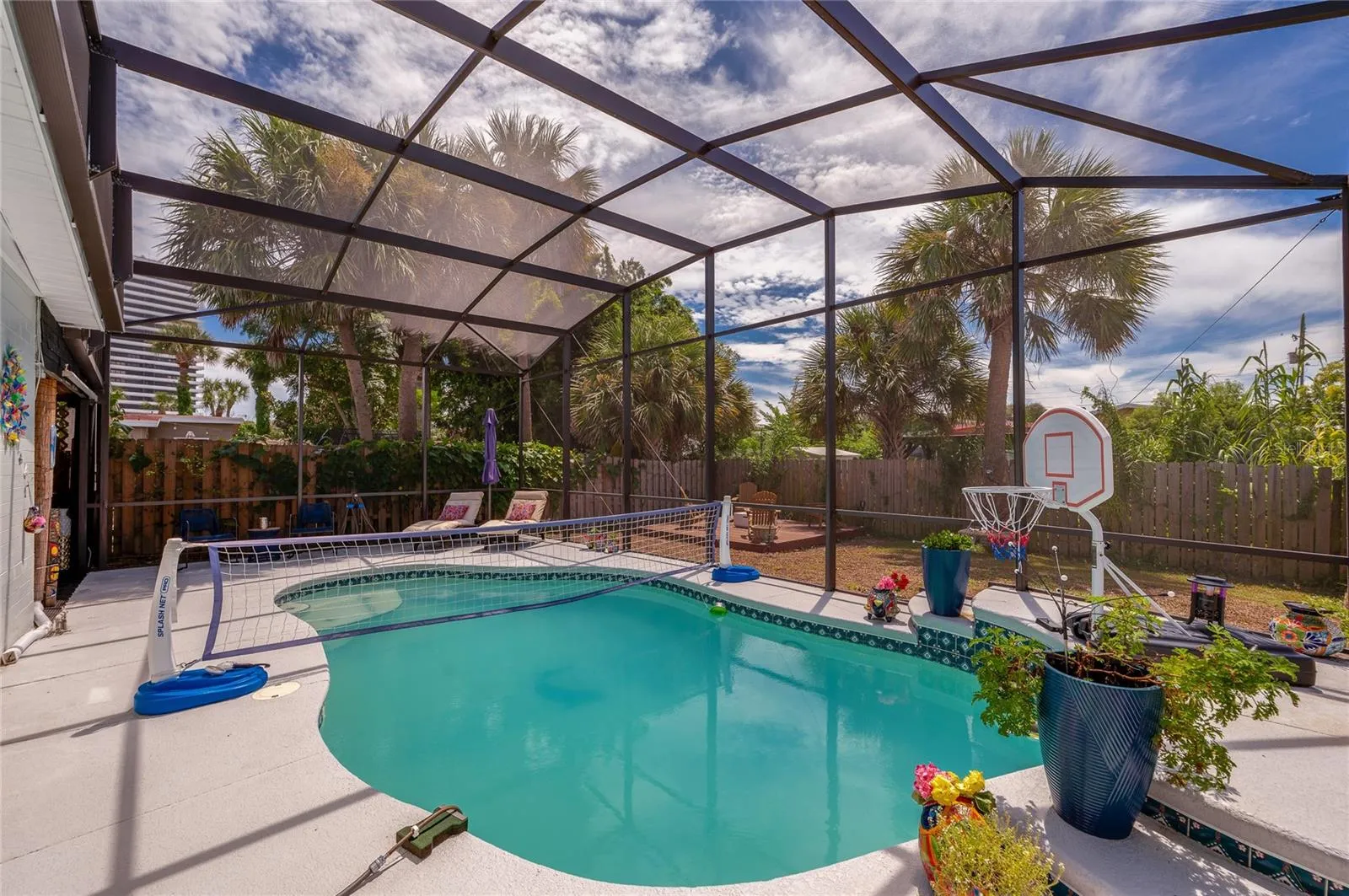 In-ground swimming pool inside a fully screened enclosure. Tiled accents and potted plants border the sunlit pool deck.
