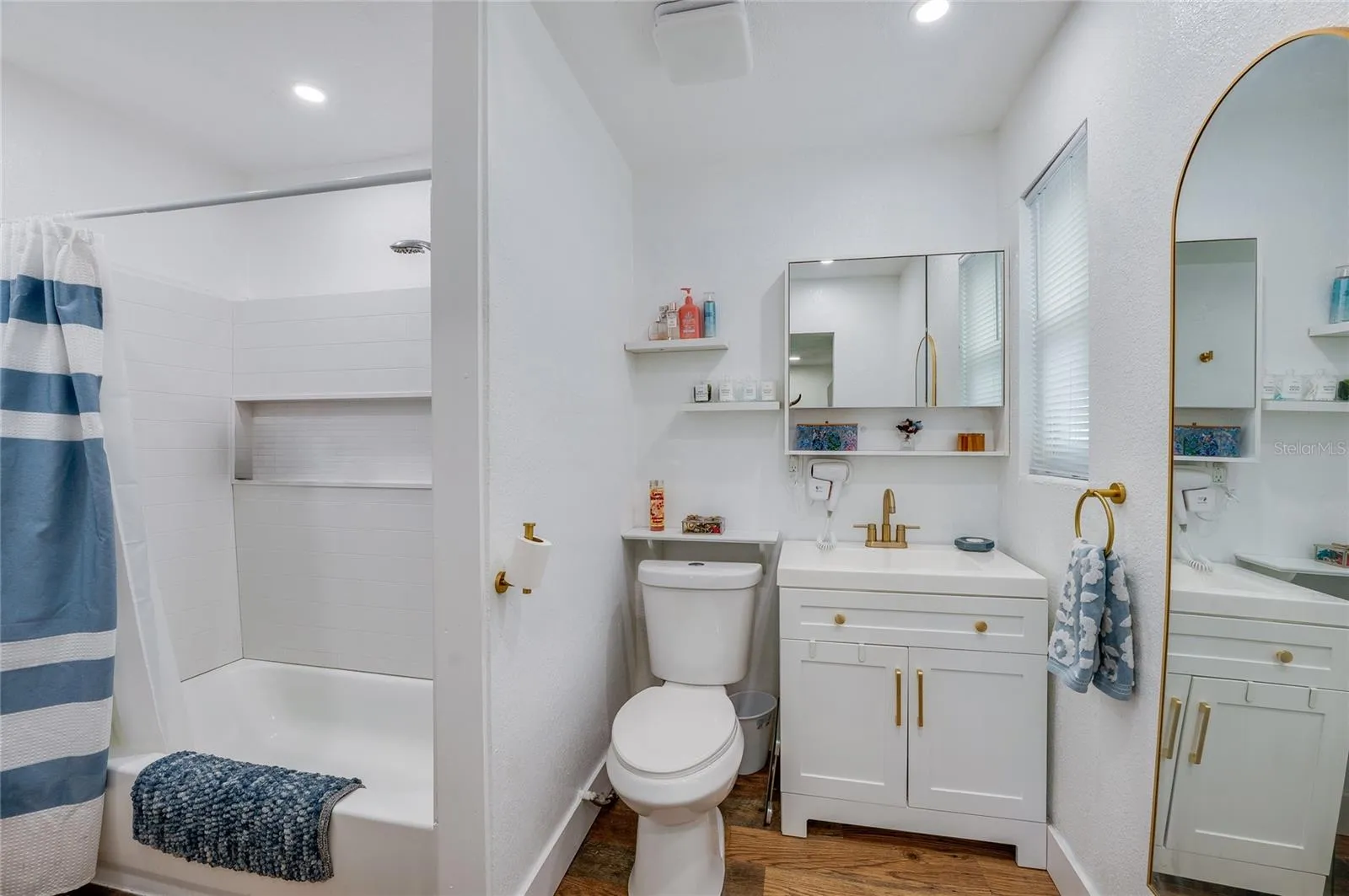 Clean full bathroom featuring a white vanity with gold hardware accents, LVP flooring, and a tub shower combination.