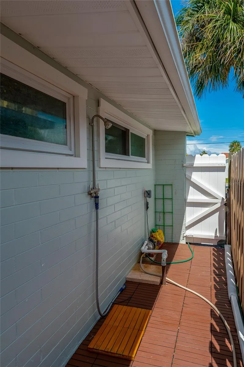 Convenient outdoor shower station installed along the side exterior wall with a wooden foot mat. A white vinyl gate provides privacy and secure access to the yard.