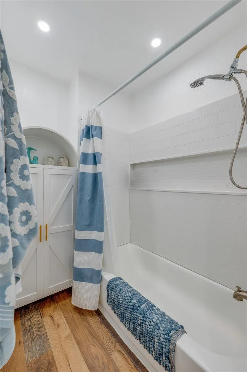 Updated bathroom display showing a white shower surround with built-in storage niches, brushed gold shower fixtures, and a white arched storage cabinet.