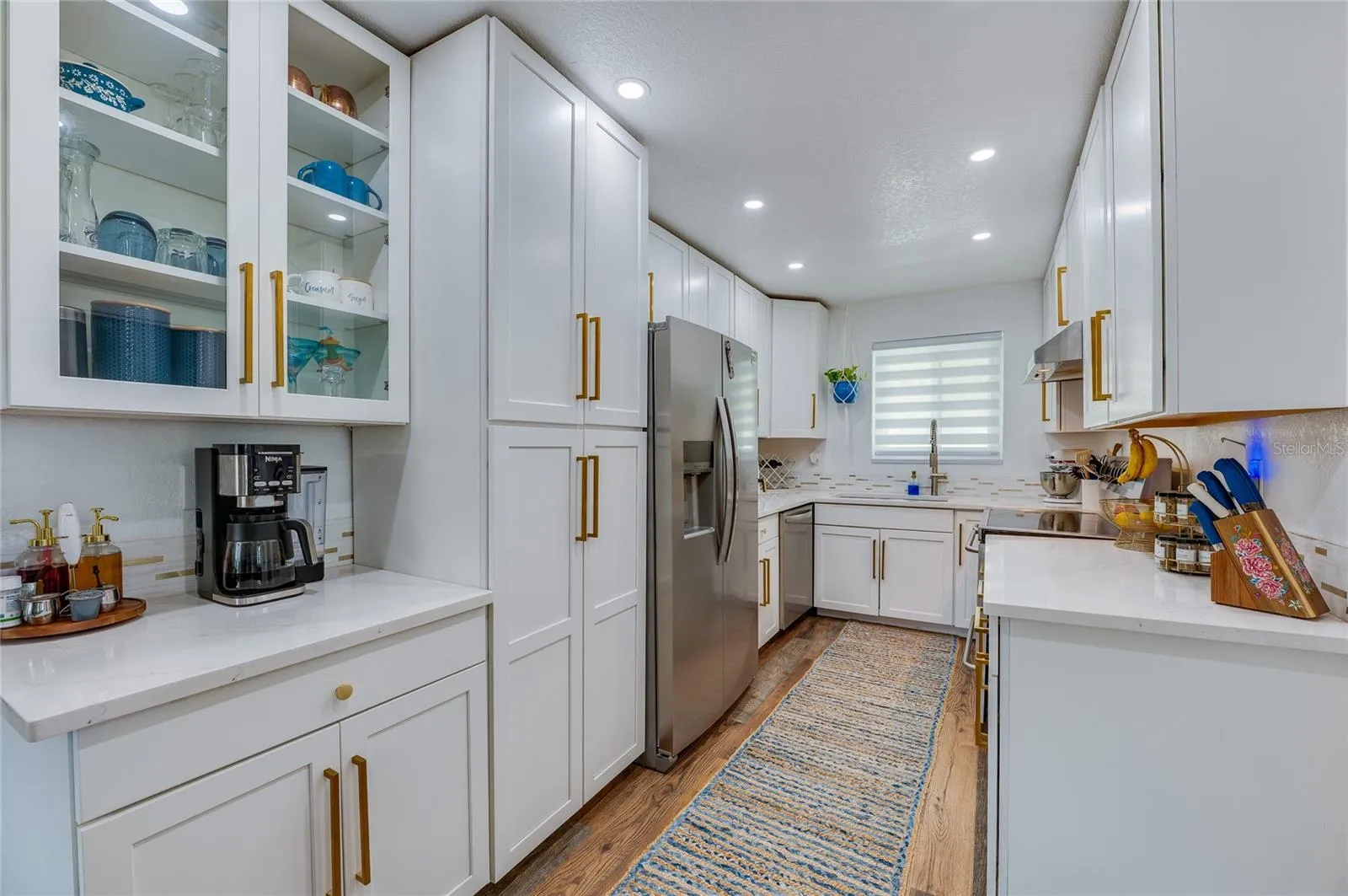 Gourmet galley kitchen featuring crisp white shaker cabinetry, gold hardware accents, stainless steel appliances, and quartz countertops.