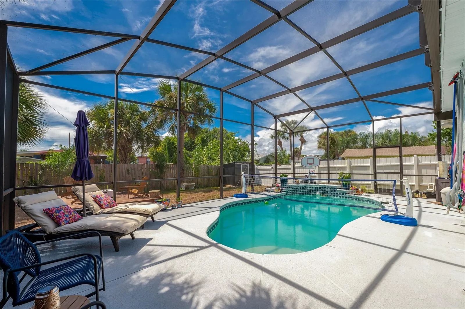 Fully screened pool enclosure featuring a crystal-clear swimming pool. Lush palm trees and a wooden fence surround the perimeter for privacy.