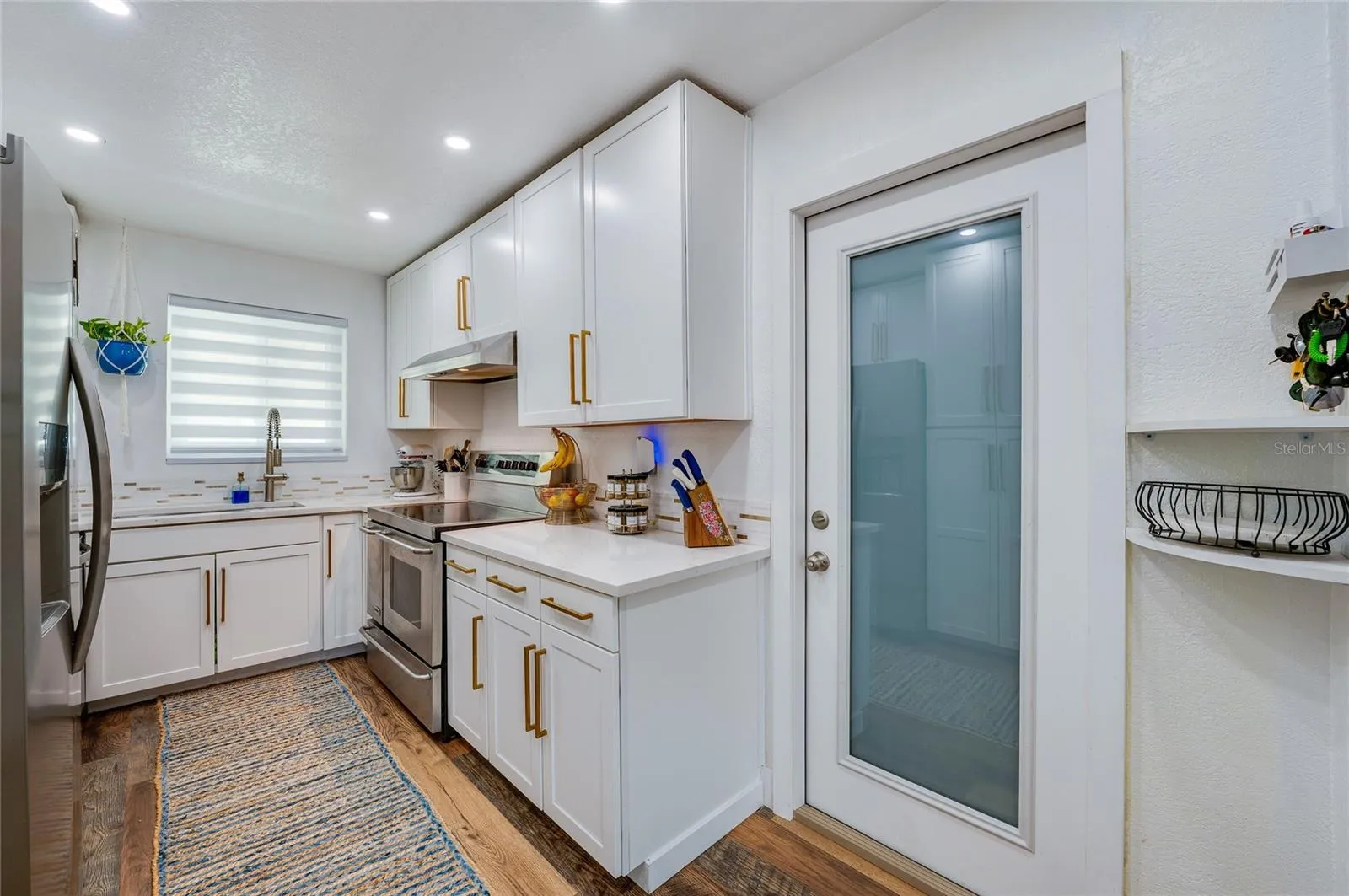 Sleek kitchen space complete with white cabinetry, warm LVP flooring, stainless steel appliances, and a glass-paneled door.
