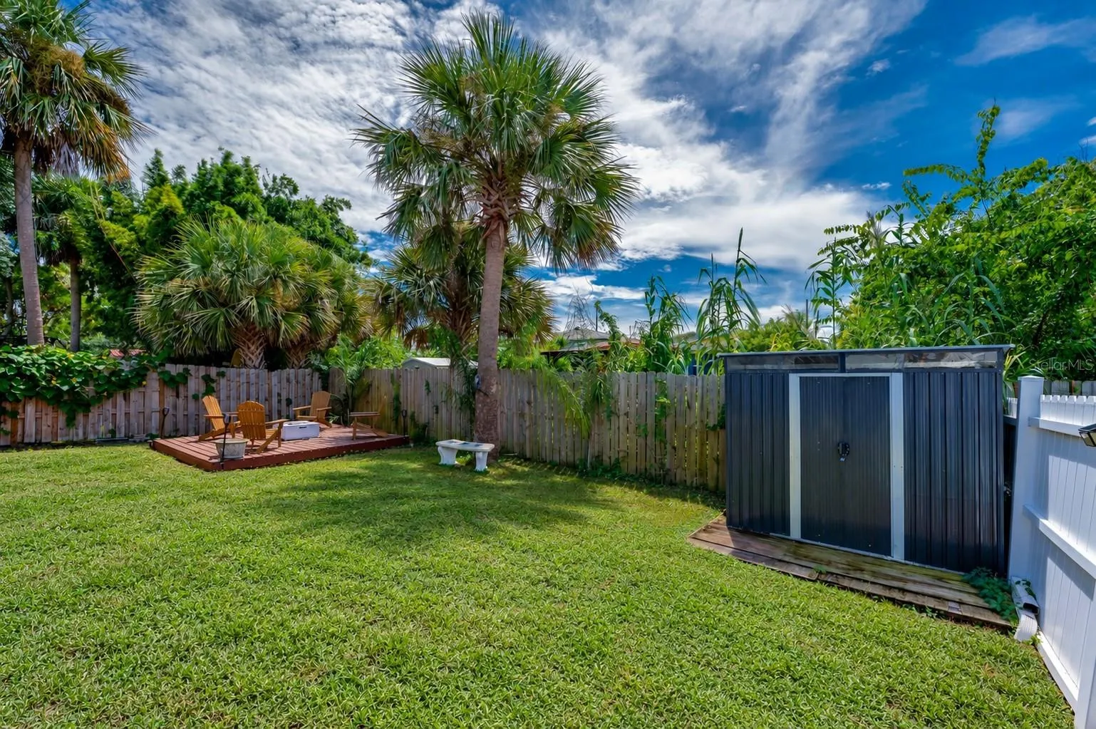 Fenced backyard area featuring a standalone storage shed and mature palm trees. A raised wooden platform sits tucked in the corner of the yard.