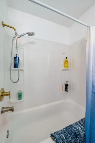 Close-up of a updated bathtub and shower combination complete with a white surround, dual wall niches for toiletries, and warm gold hardware.