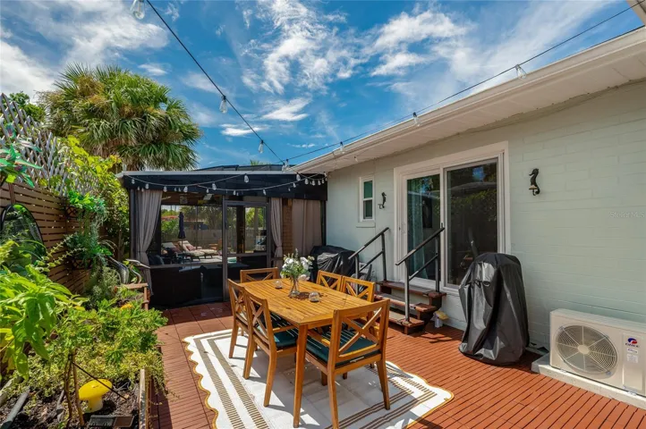 Spacious outdoor patio area with dark wooden decking, sliding glass door access, and string lights overhead. The space includes raised garden planters and a adjacent screen enclosure.