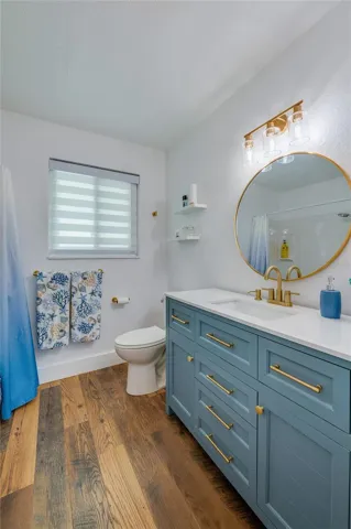 Stylish bathroom featuring a blue vanity with gold hardware, a round brass-framed mirror, and modern lighting.