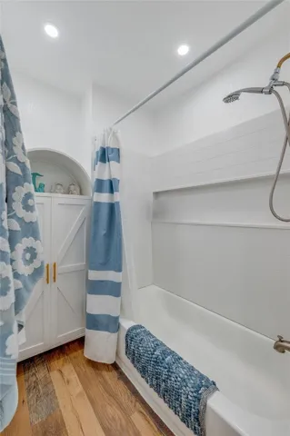 Updated bathroom display showing a white shower surround with built-in storage niches, brushed gold shower fixtures, and a white arched storage cabinet.