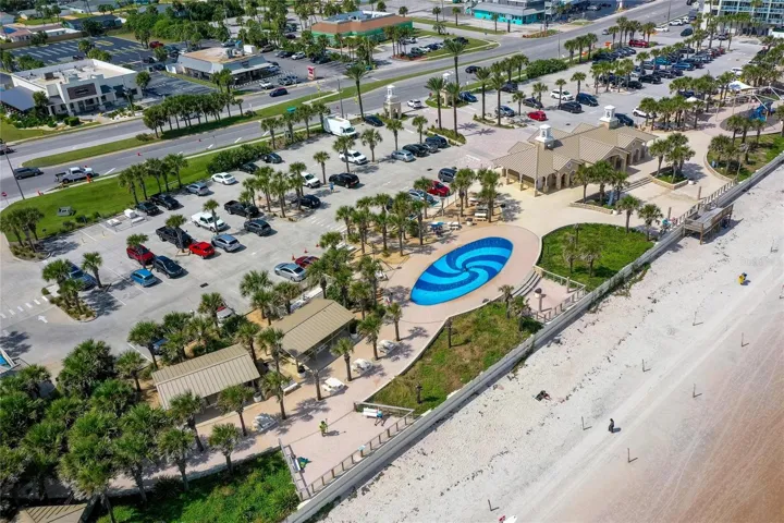 Sweeping aerial view captures Andy Romano Beachfront Park along the Atlantic coastline, featuring beachfront recreation areas, landscaped grounds, parking, and direct access to the sand.