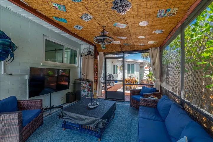 Inviting screened-in patio area with decorative bamboo ceiling panels and sheer privacy curtains. It offers clear views leading out to the sunlit outdoor deck.