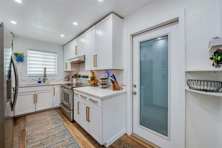 Sleek kitchen space complete with white cabinetry, warm LVP flooring, stainless steel appliances, and a glass-paneled door.