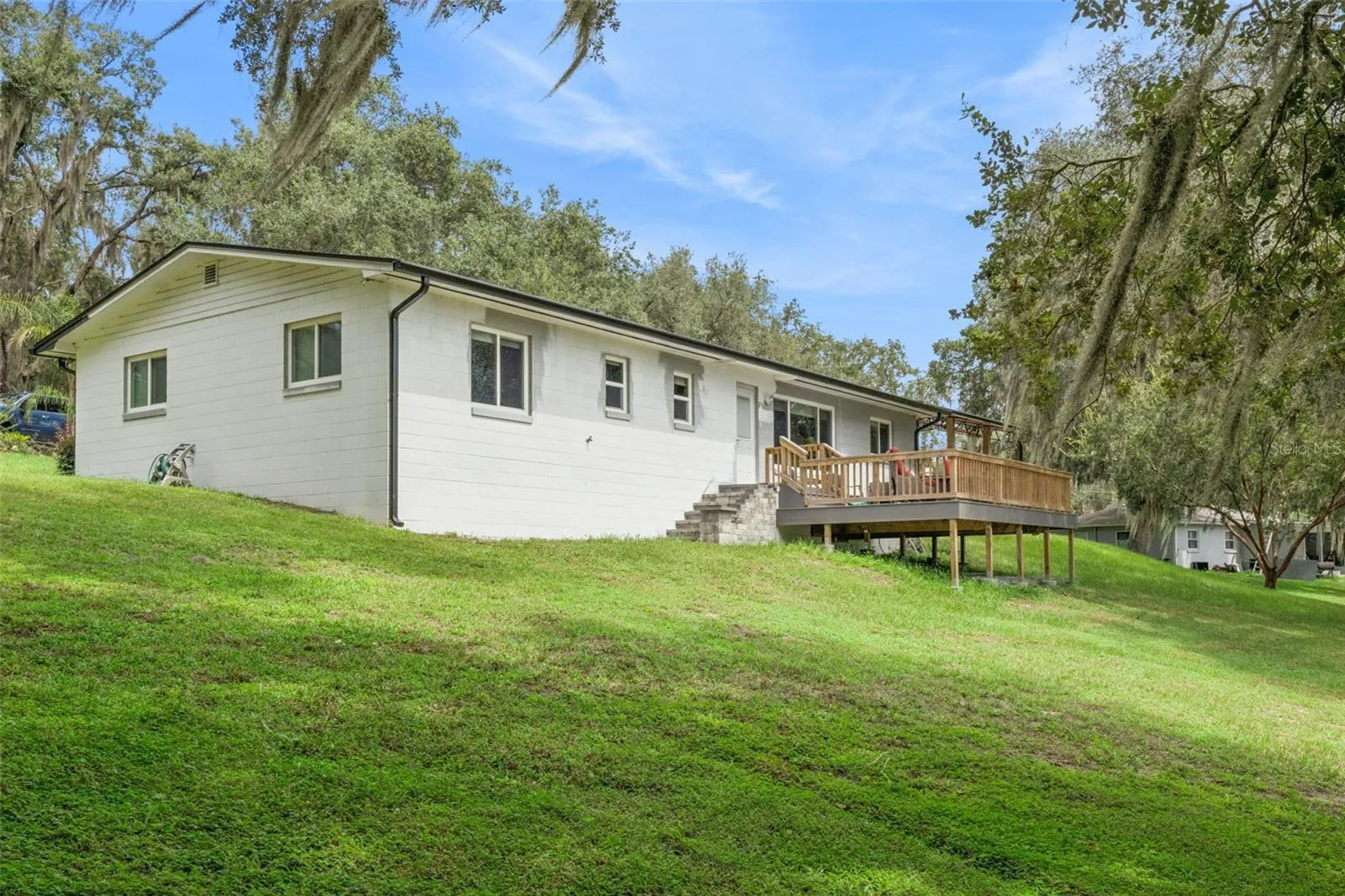 Rear view of the home showcasing the elevated deck, manicured lawn, and the natural beauty of Central Florida's rolling landscape.