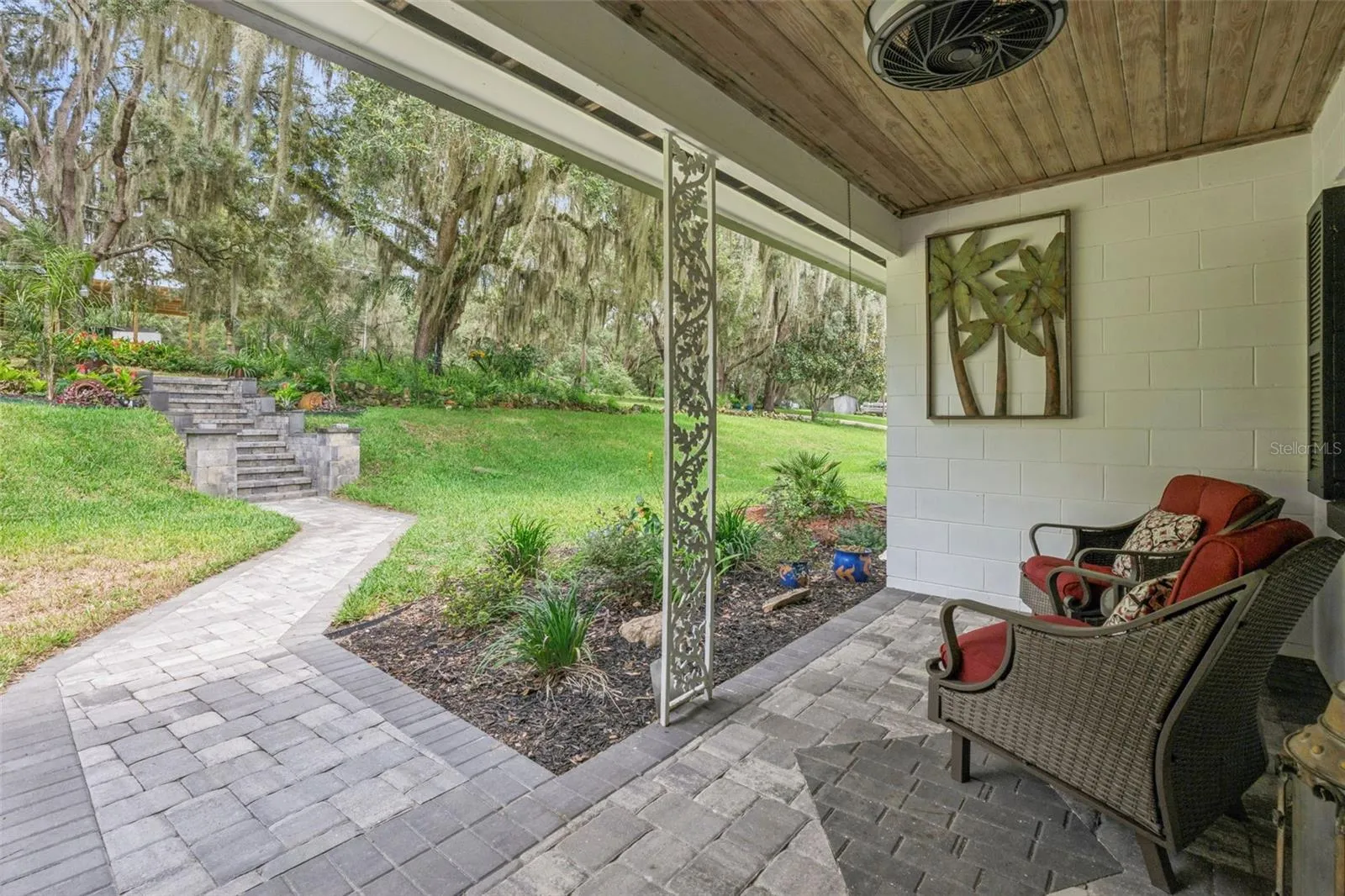Covered lower patio with paver stone flooring, a decorative trellis, and a paver walkway leading through the lush, shaded yard.