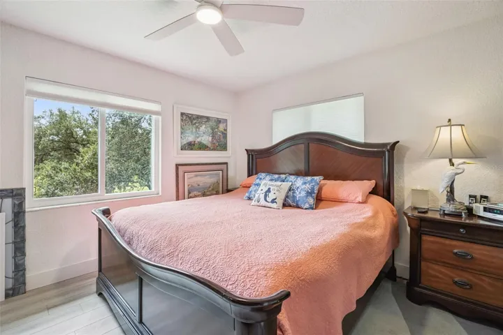 Retreat to the relaxing primary suite featuring a cozy fireplace accent, ceiling fan, and serene tree-top views through oversized windows.