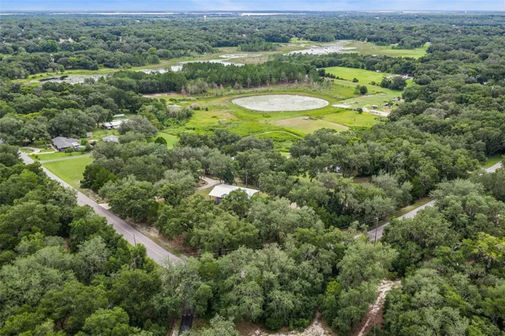Drone view capturing the home's ideal positioning among towering oaks with expansive views of surrounding farmland.