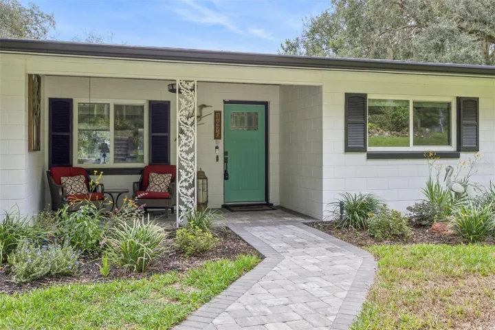Step onto the welcoming front porch featuring paver stone, comfortable seating, and lush garden views.