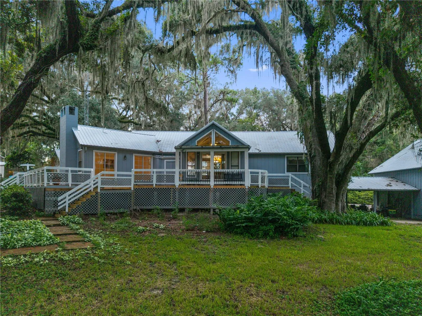 Rear exterior of the home featuring an expansive deck surrounded by majestic oak trees and lush landscaping.