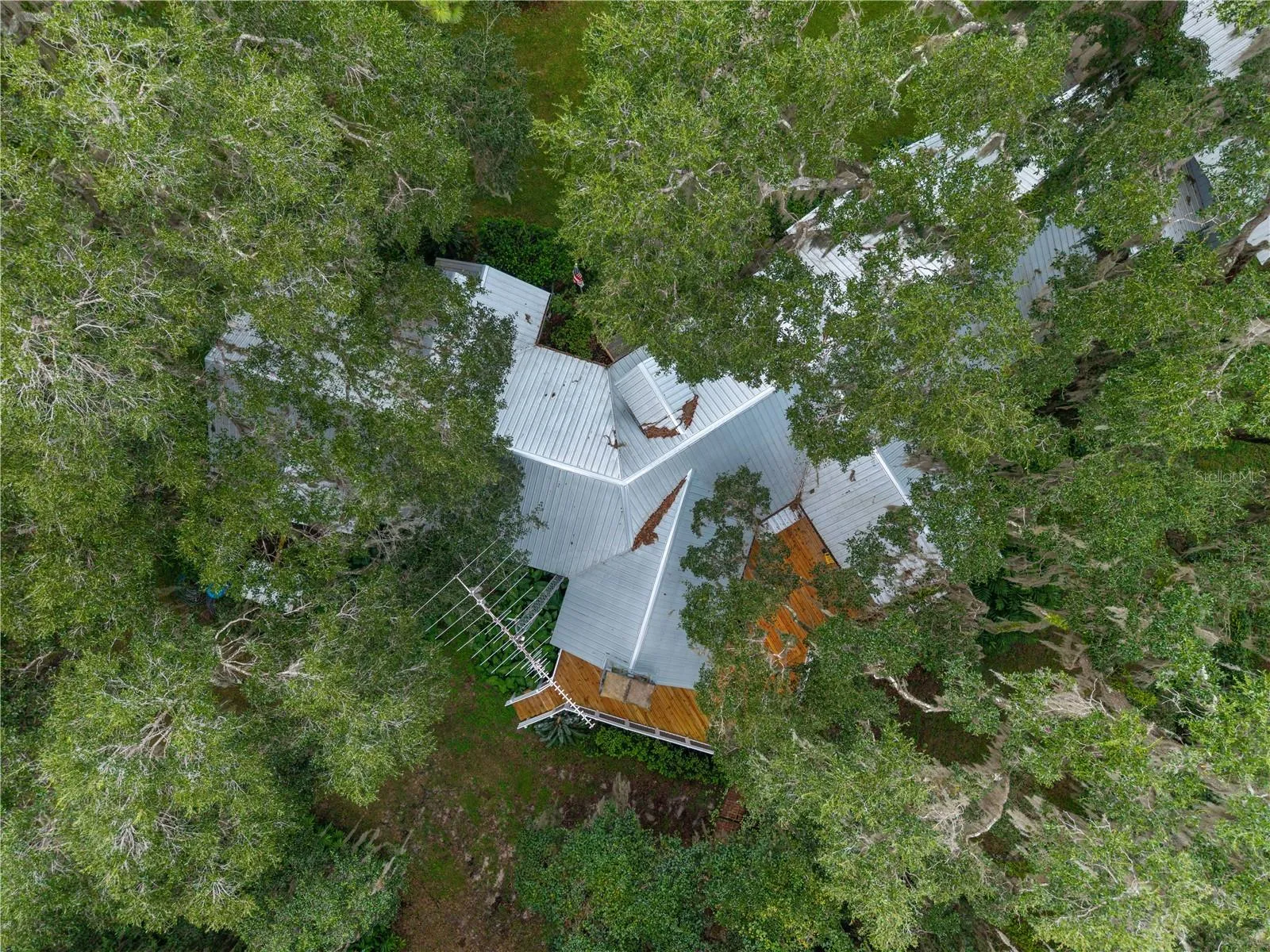 Aerial view of the home nestled among mature trees, showcasing the metal roof and surrounding decks.