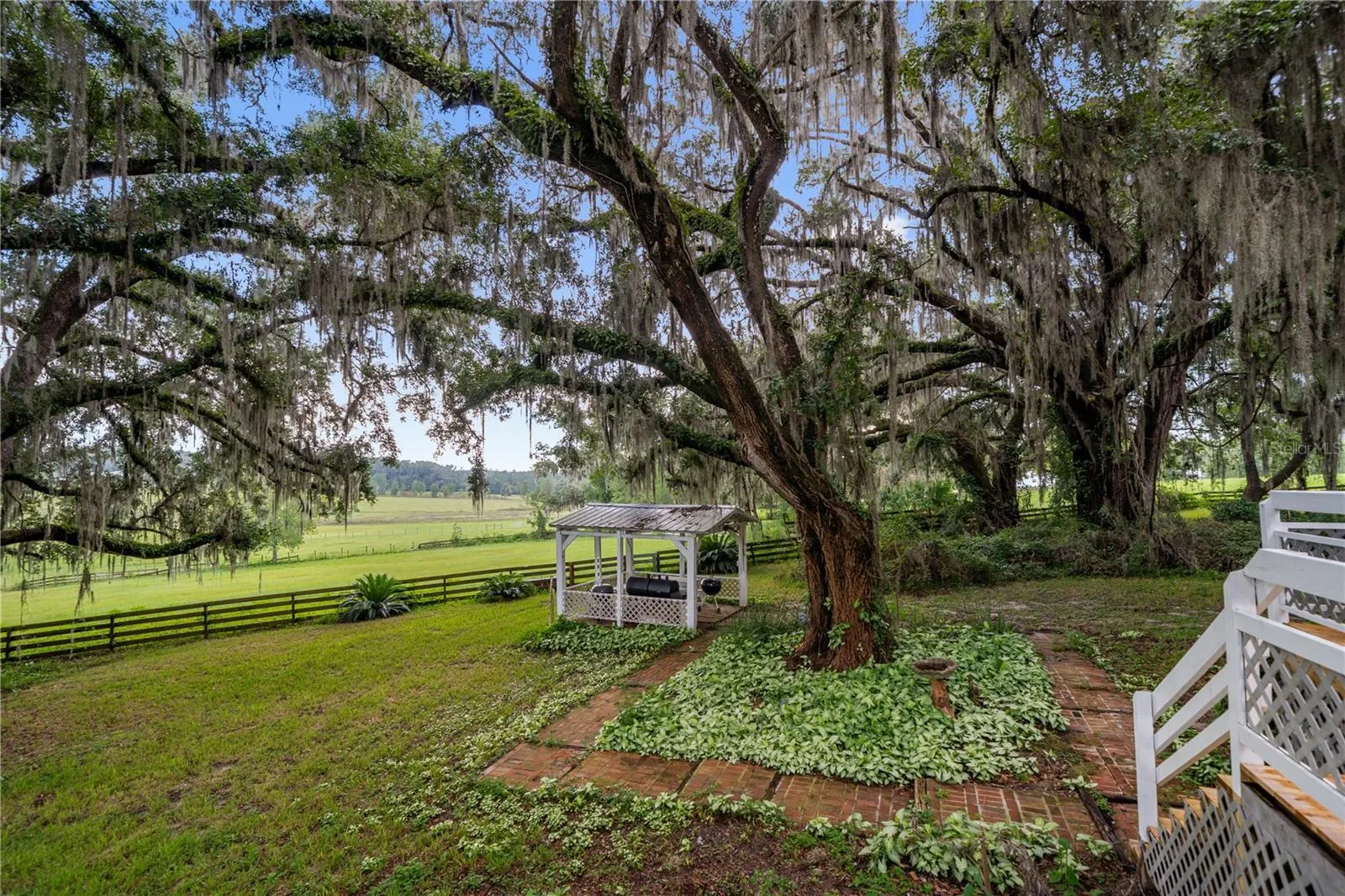 Beautiful backyard shaded by majestic oak trees draped in Spanish moss, featuring a charming gazebo and peaceful views of the surrounding pasture.