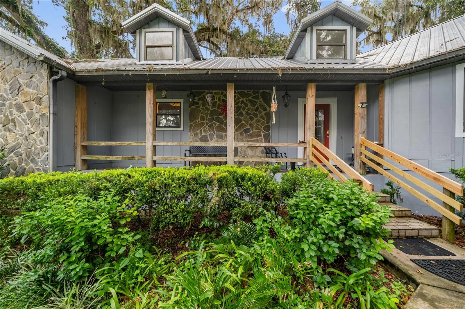 Front exterior featuring a spacious covered porch, stone accents, and mature landscaping.