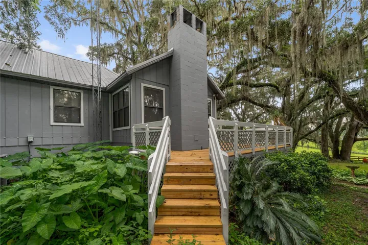 Rear exterior featuring a spacious elevated deck surrounded by mature trees and lush landscaping.