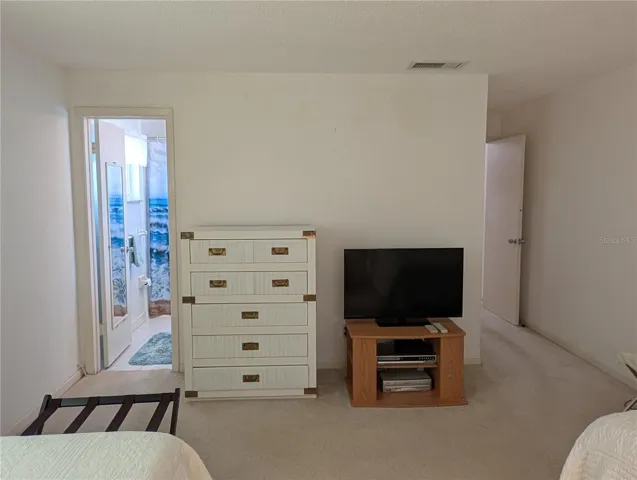View thru primary bedroom to bathroom and entry to hall.  Walk-in closet as you exit (wall behind TV).