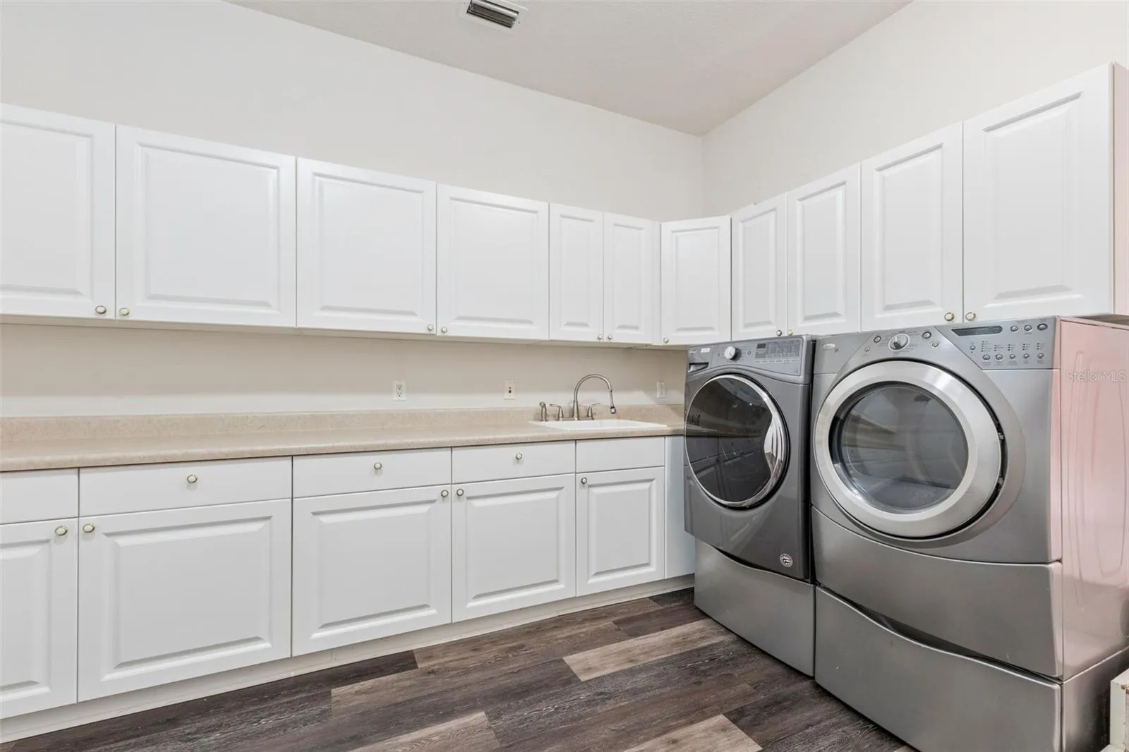 Oversized laundry room with extensive cabinetry, countertop workspace, and utility sink.