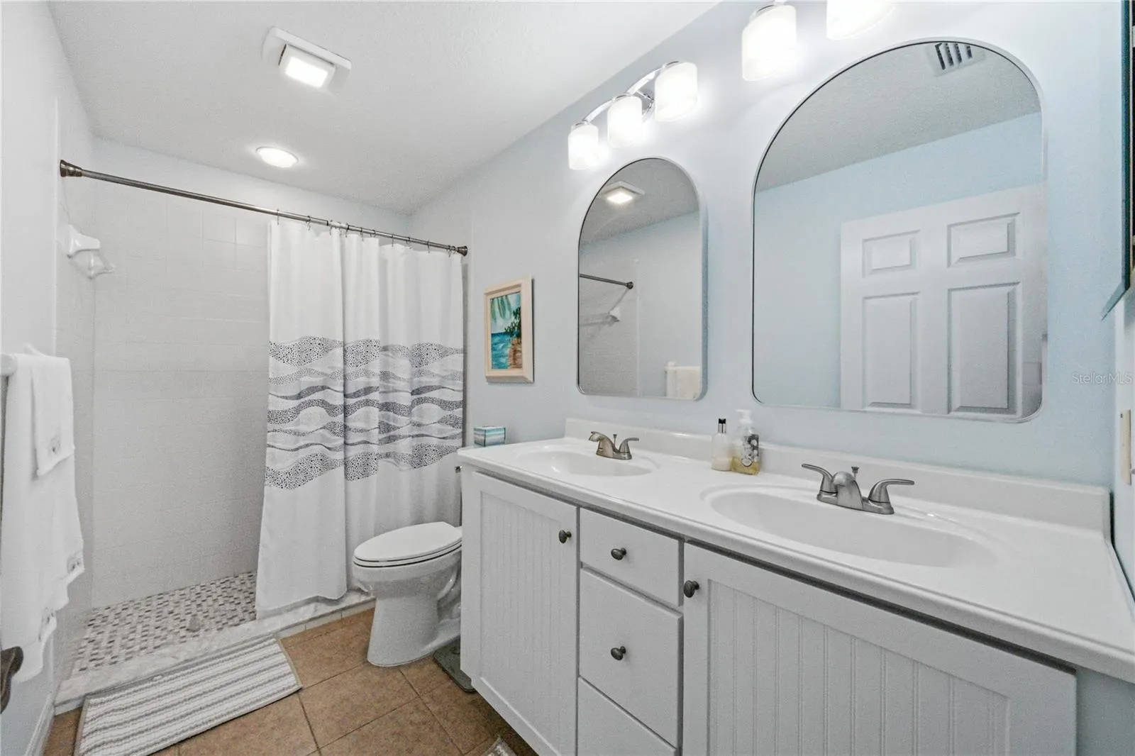 The recently remodeled primary bathroom has a large stall shower with ceramic tile surround, elevated vanity with 2 sinks in a stone counter, elongated stool, upgraded lighting, plumbing and mirrors.